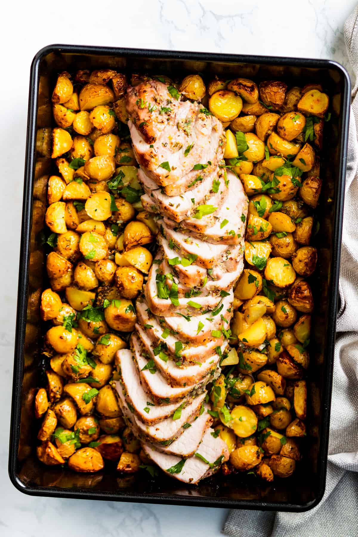 overhead shot of black baking pan with Baked honey garlic pork tenderloin with roasted potatoes, garnished with parsley.