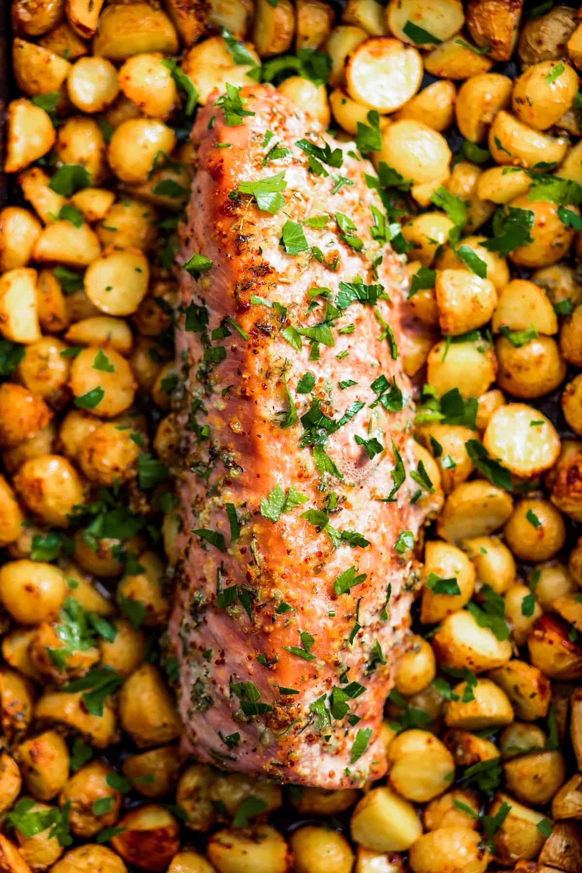 Baked honey garlic pork tenderloin with roasted potatoes, garnished with parsley.