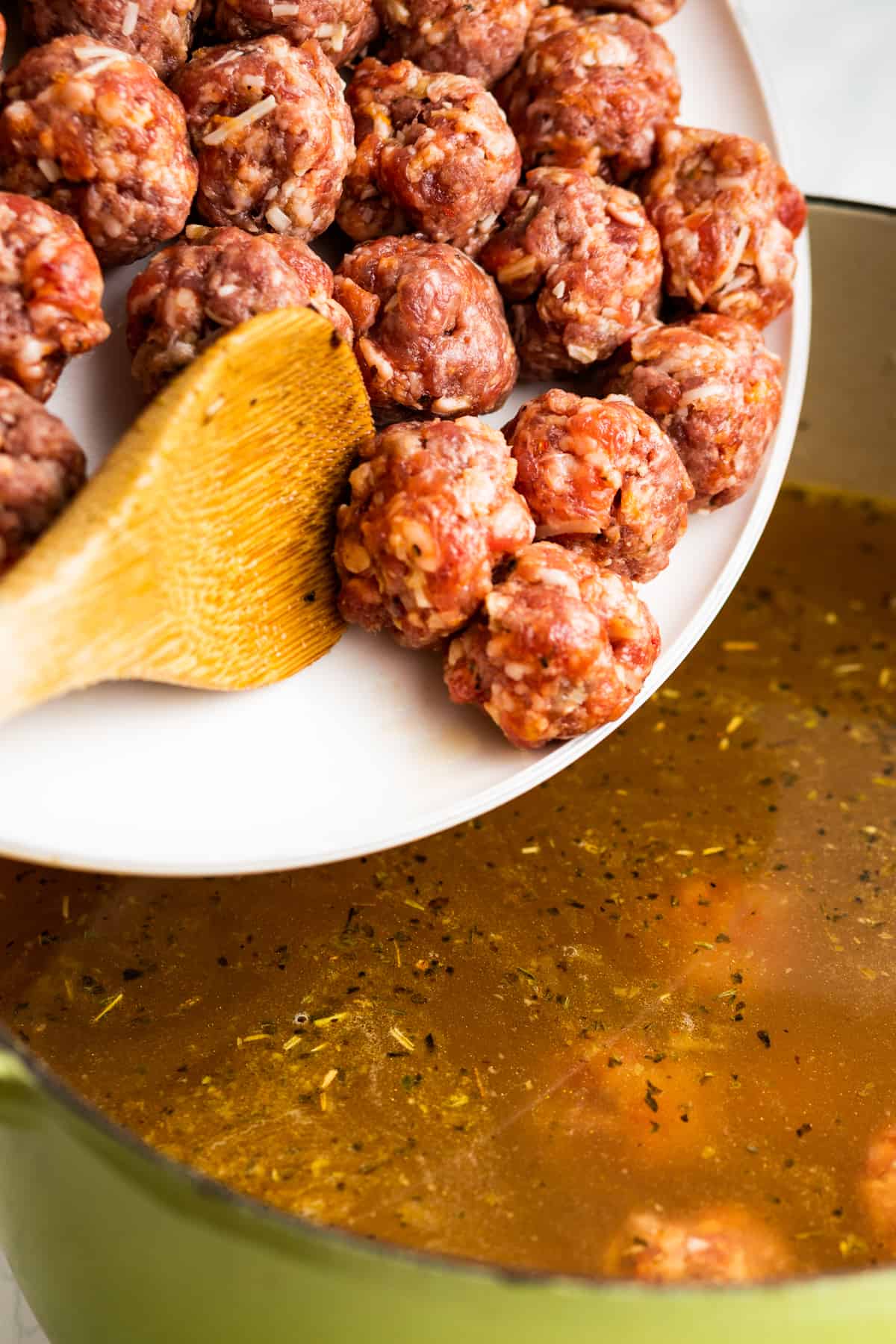 adding raw meatballs to broth in a soup pot.