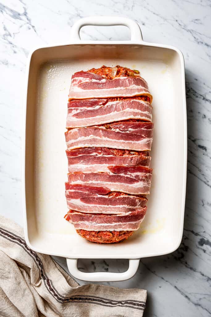 Bacon slices draped over an unbaked meatloaf.