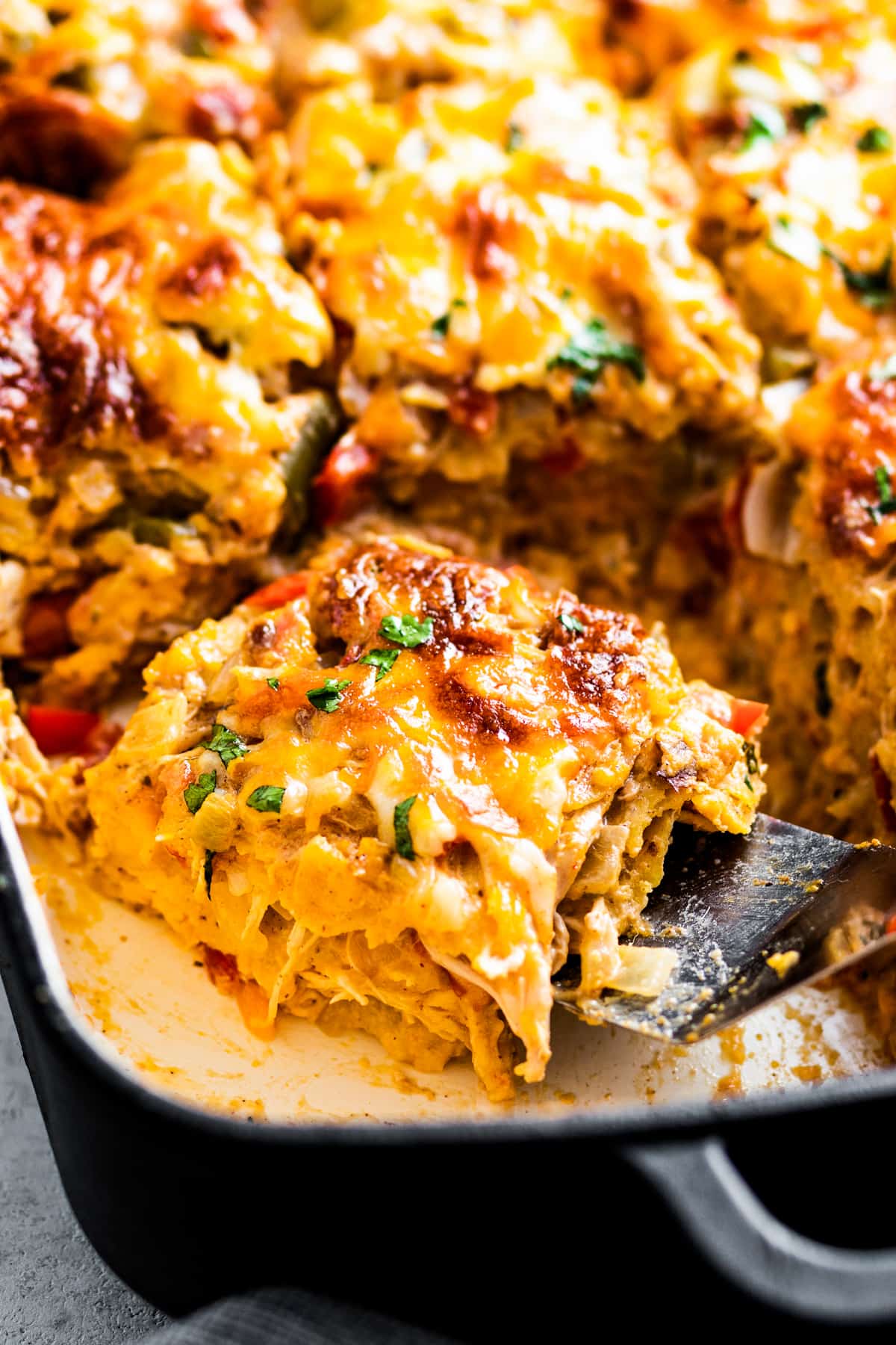 side shot of sliced king ranch chicken casserole, with a slice set on top of a metal spatula.