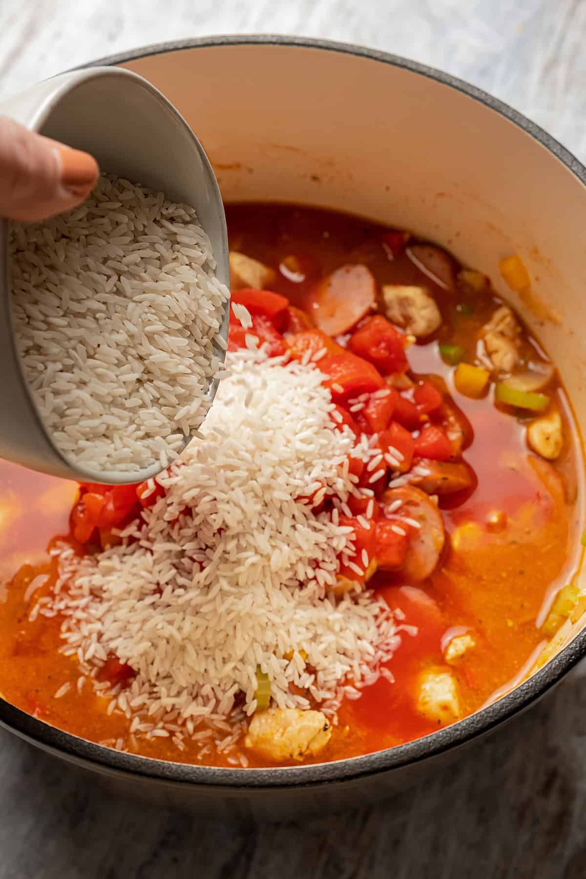 Pouring rice into Dutch oven with jambalaya ingredients