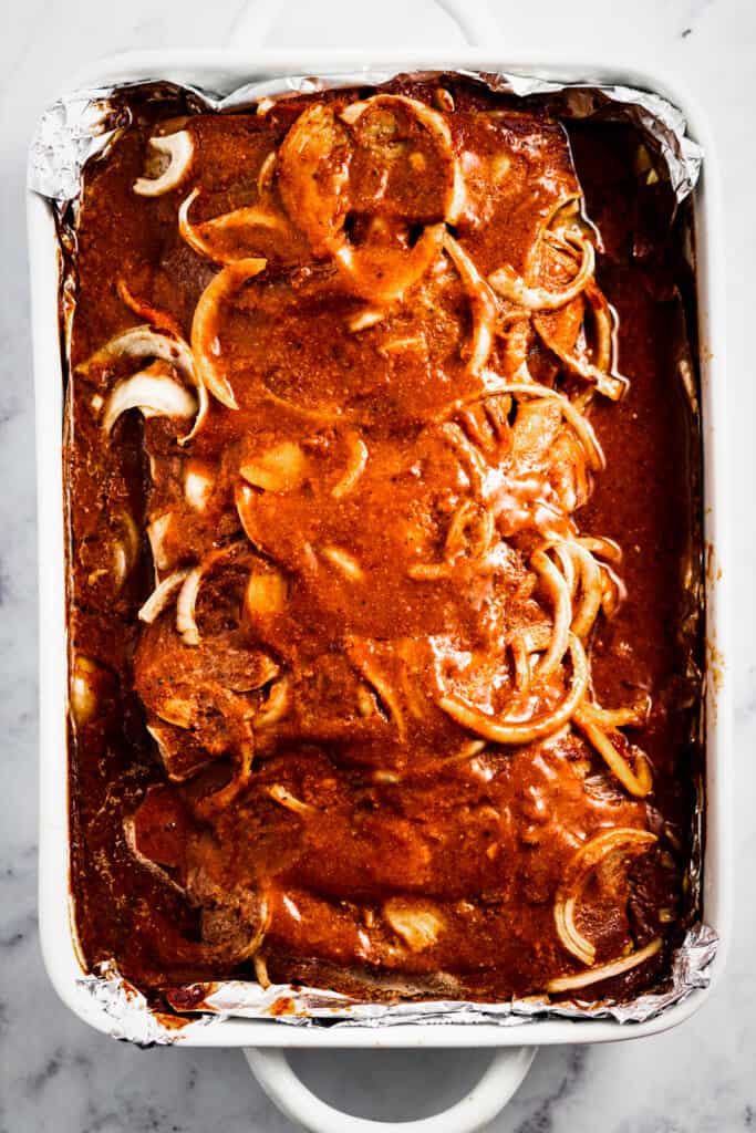 Baked ribs in a sauce with sliced onions on top.
