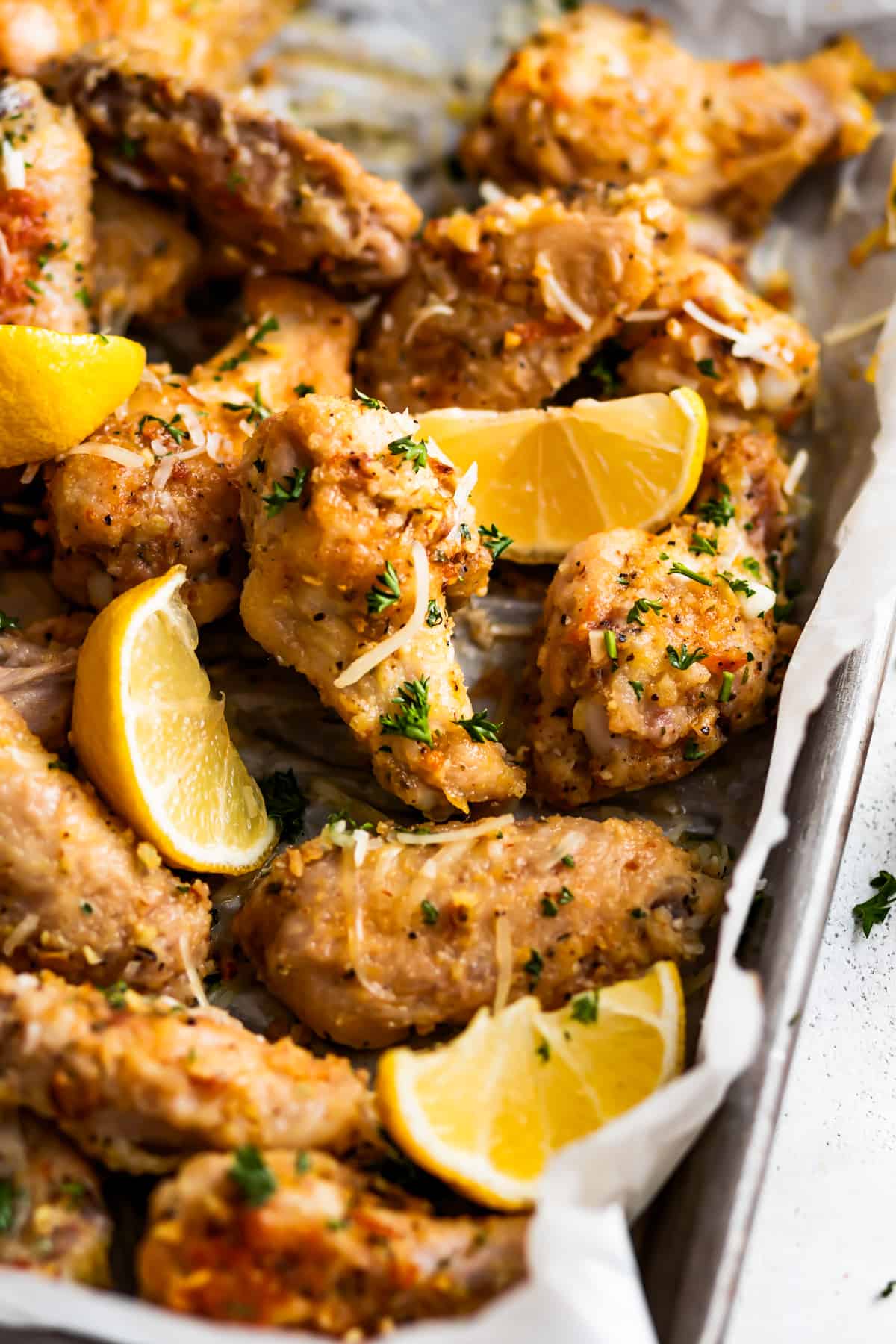 Angled photo of lemon pepper chicken wings, with lemon wedges arranged over the wings.
