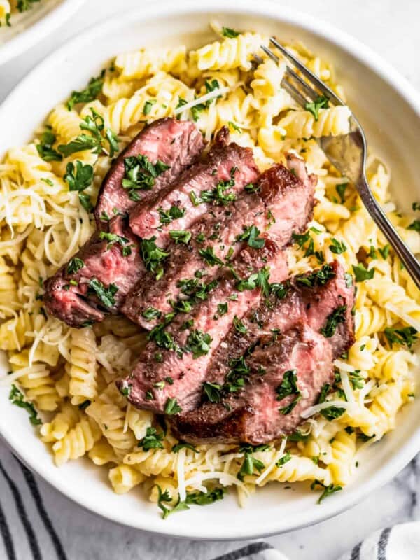 Overhead shot of a sliced steak arranged over Alfredo pasta in a bowl.