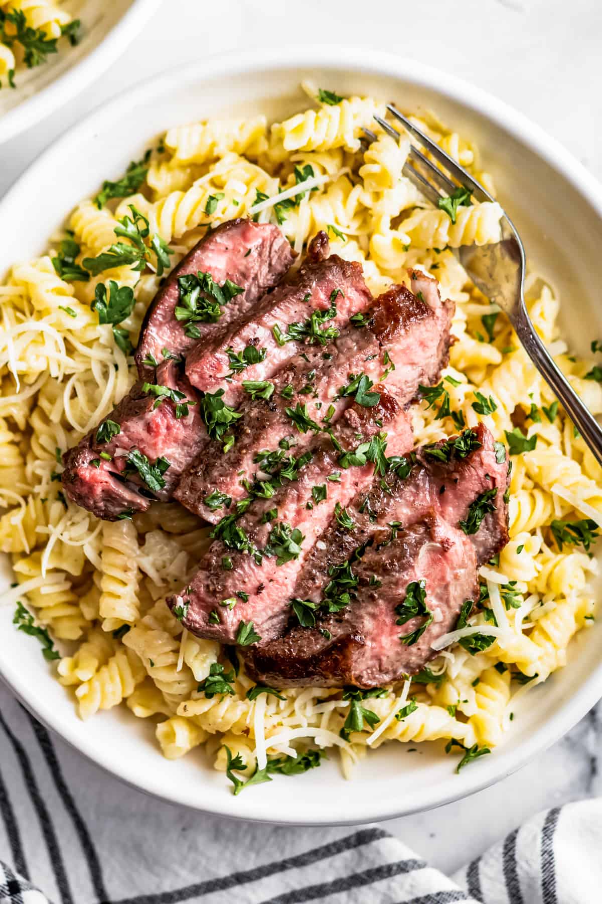 Overhead shot of a sliced steak arranged over Alfredo pasta in a bowl.