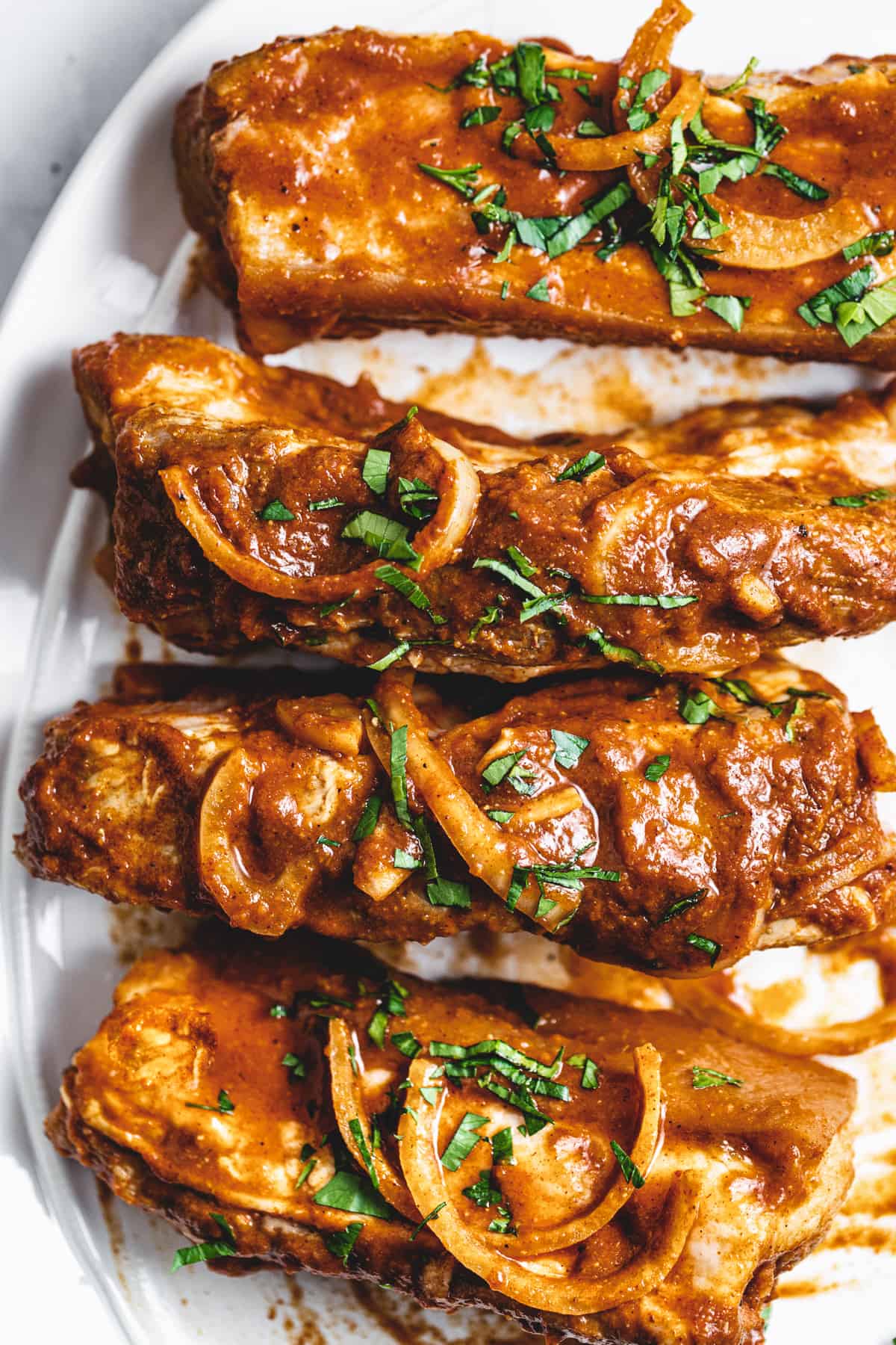 serving plate holding four country style pork ribs with onions and cilantro on top.