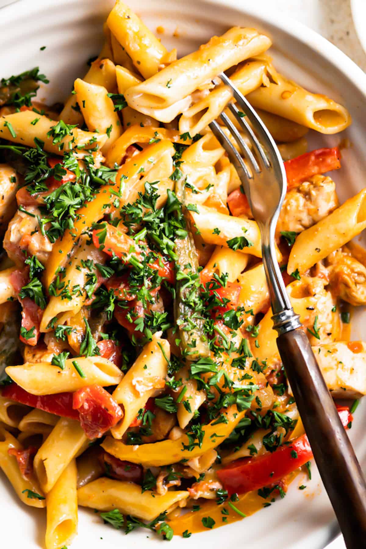 close up overhead shot of a bowl with jerk chicken pasta with parsley on top.