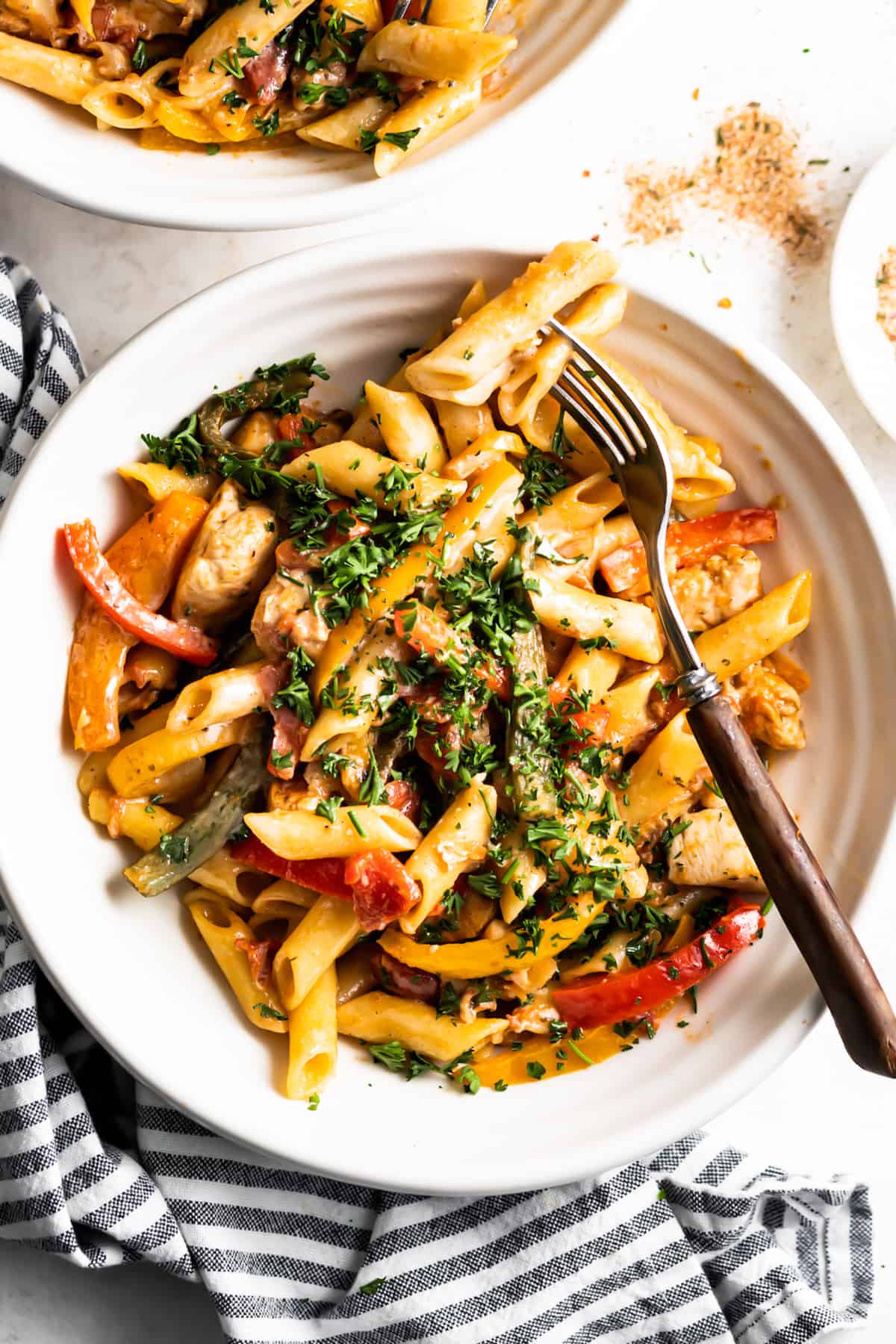 overhead shot of a bowl with jerk chicken and pasta with chopped parsley on top, and a fork set on the right side of the bowl.