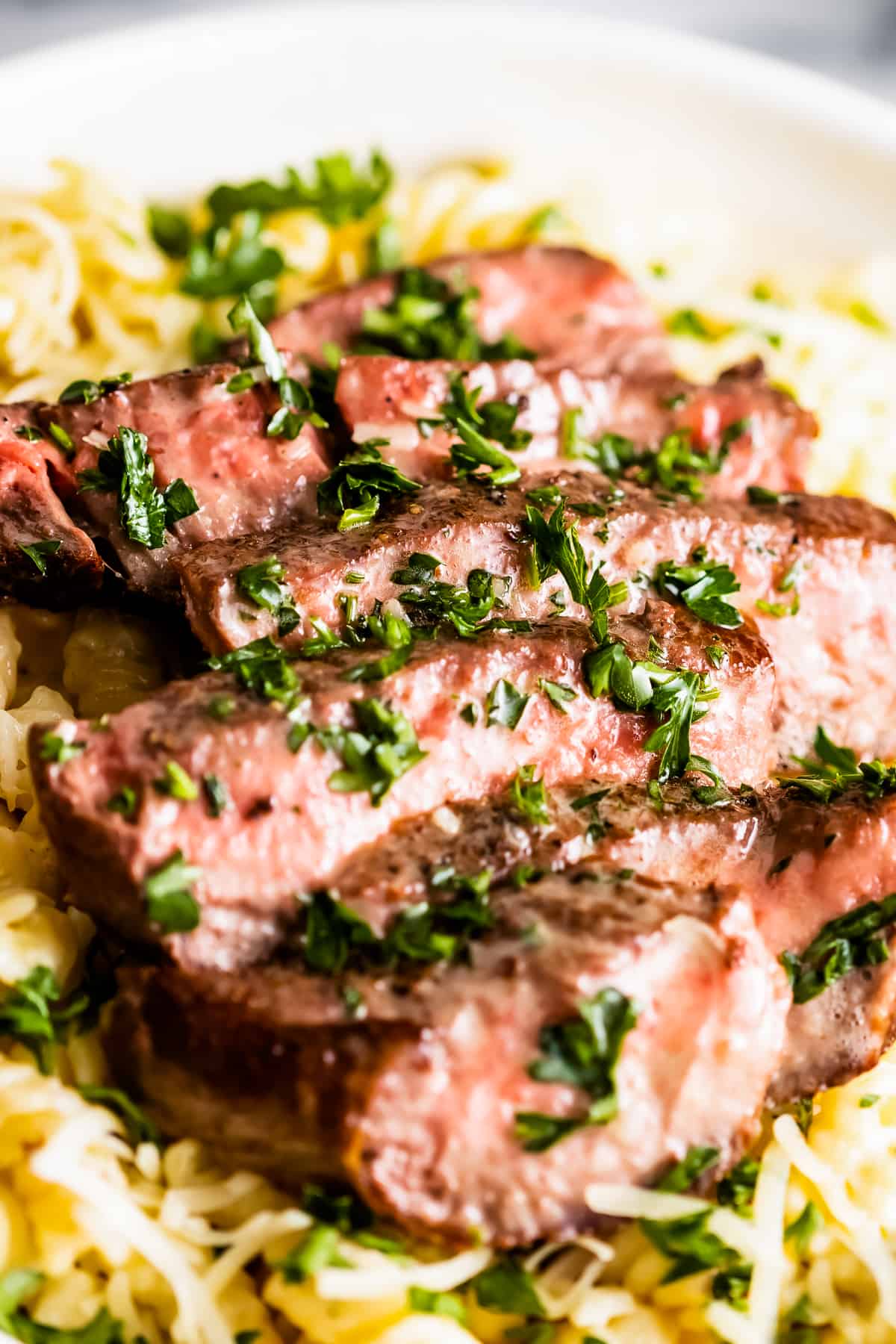 Up close shot of sliced ribeye steak served over fusilli pasta.