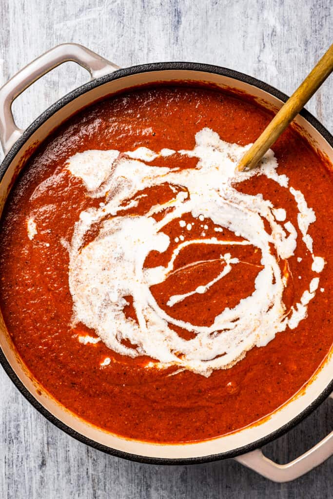 Adding the heavy cream-cornstarch slurry to a tomato soup.
