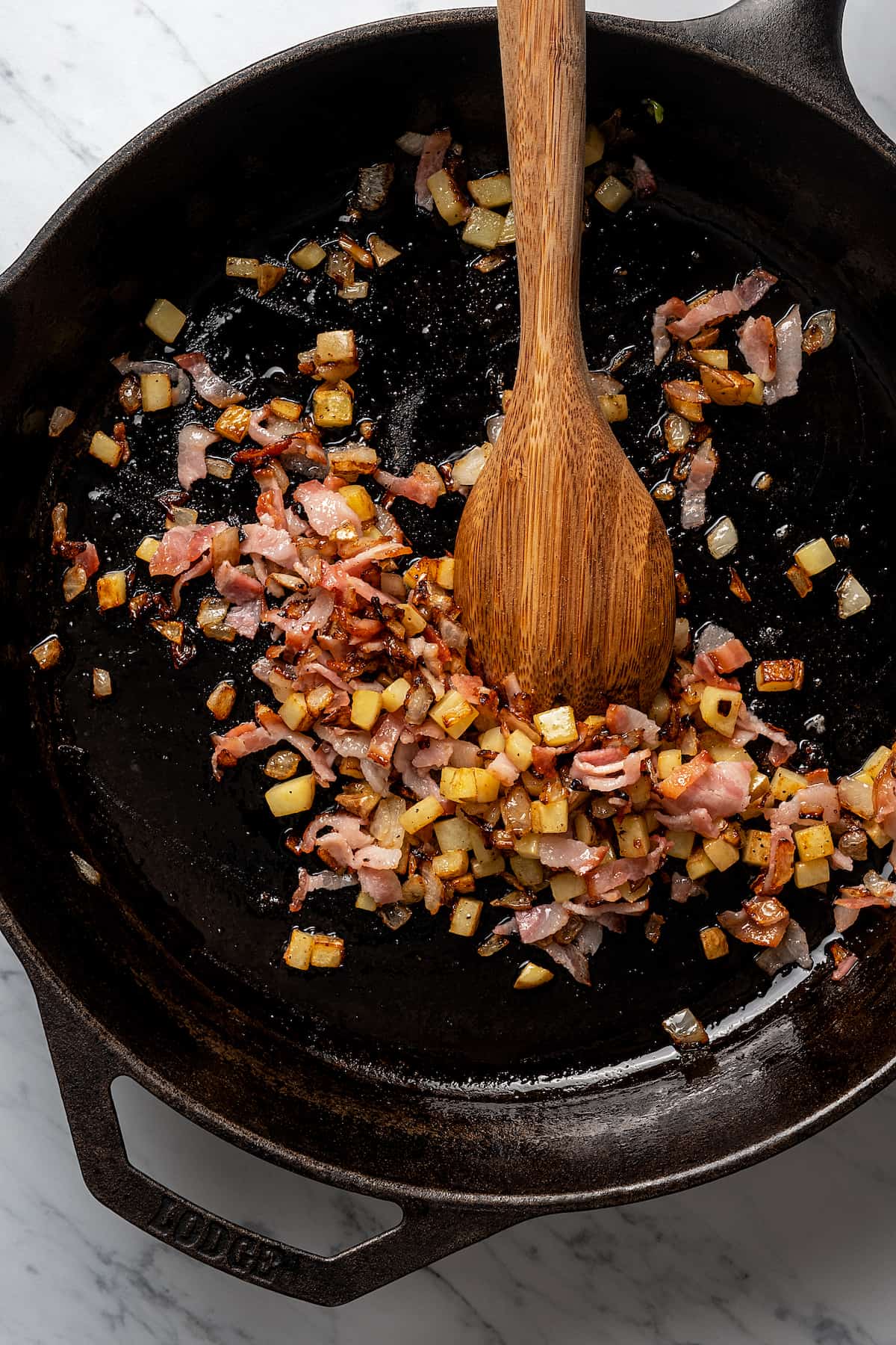 Adding the crushed bacon into the pan with onions and potatoes. 