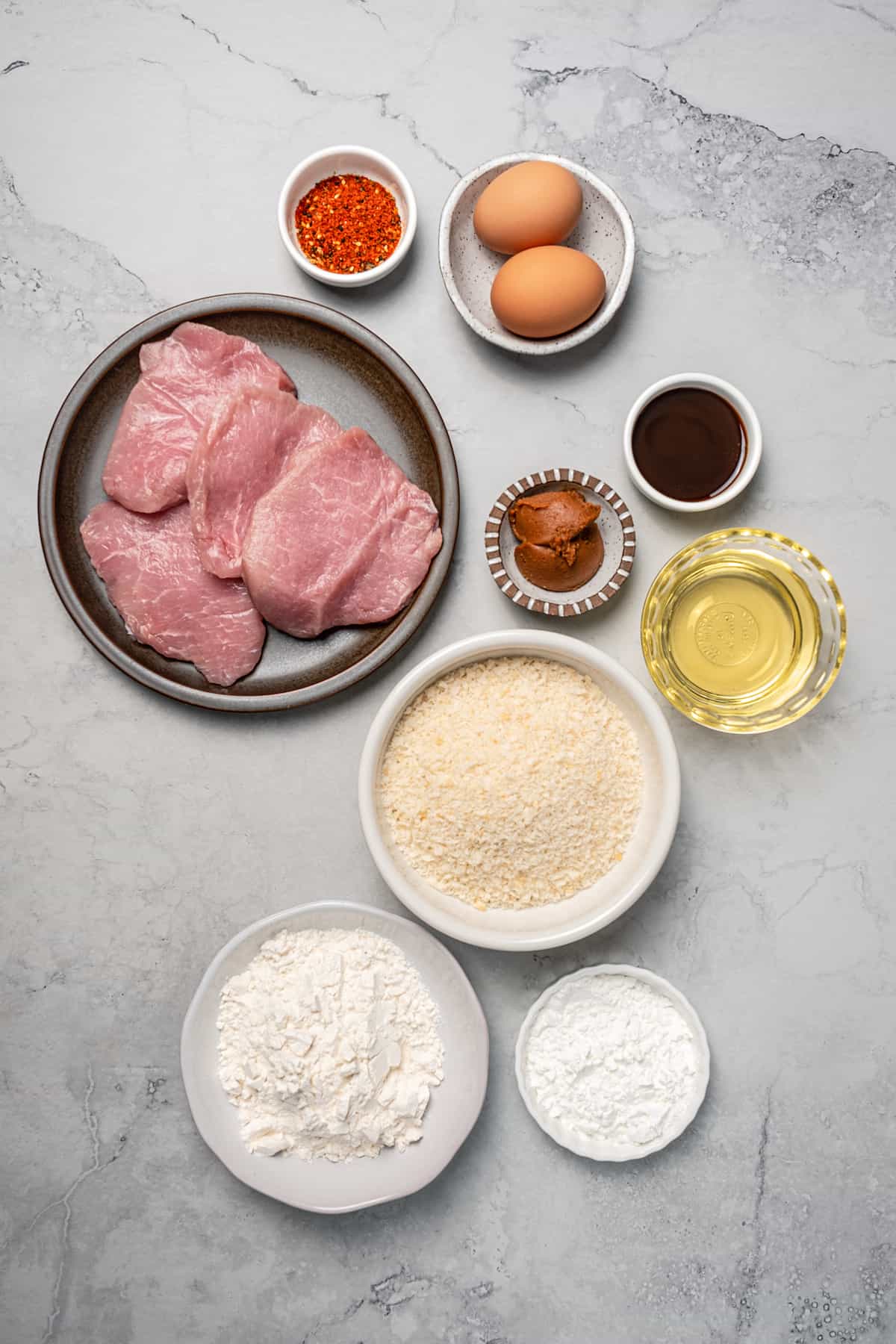 The ingredients for pork katsu measured and arranged in dishes on a work surface.