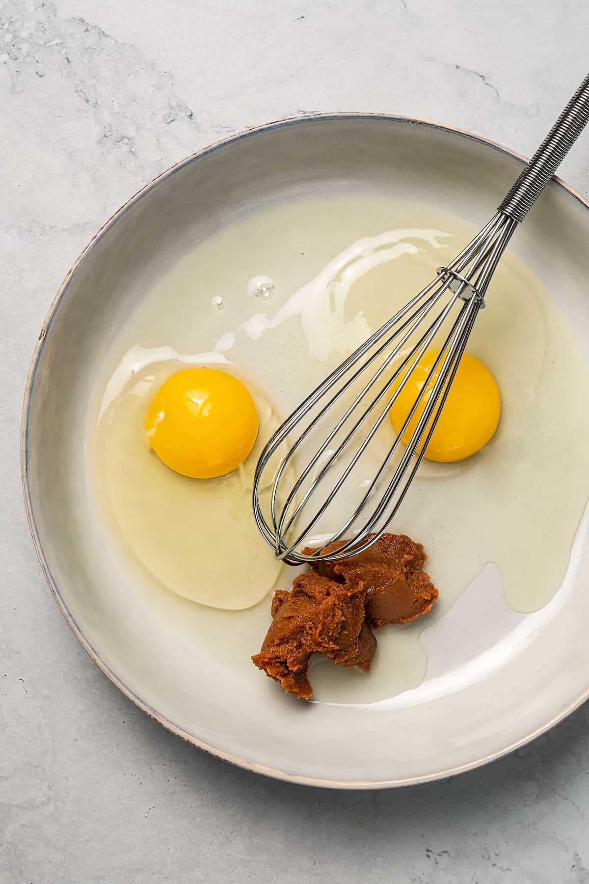 Eggs and red miso in a bowl with a whisk.