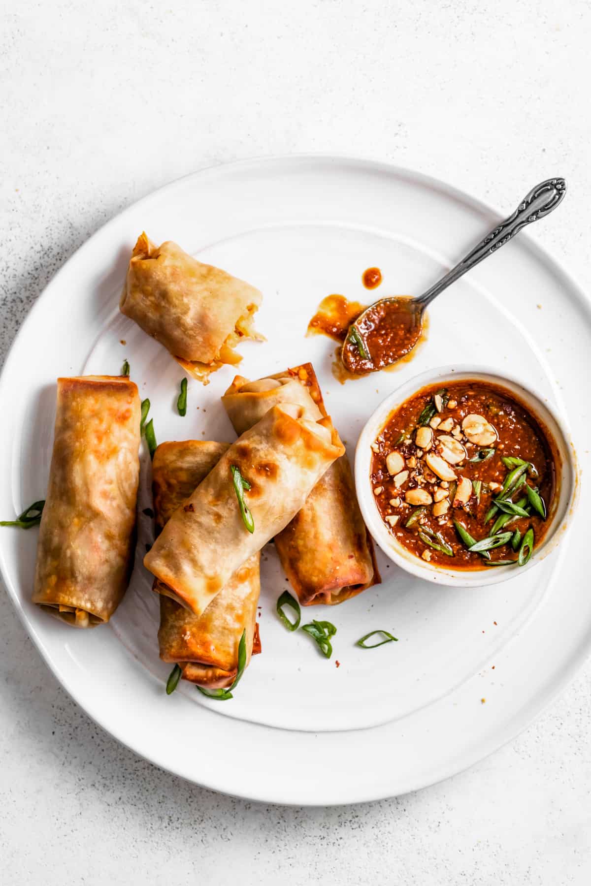 Air fryer spring rolls with peanut sauce served on a white plate.