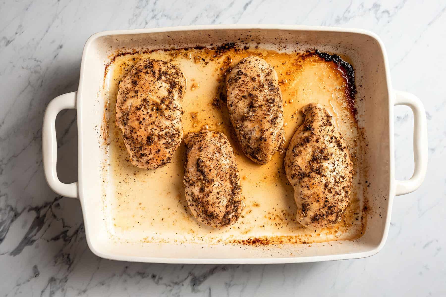 Four baked chicken breasts in a casserole dish.