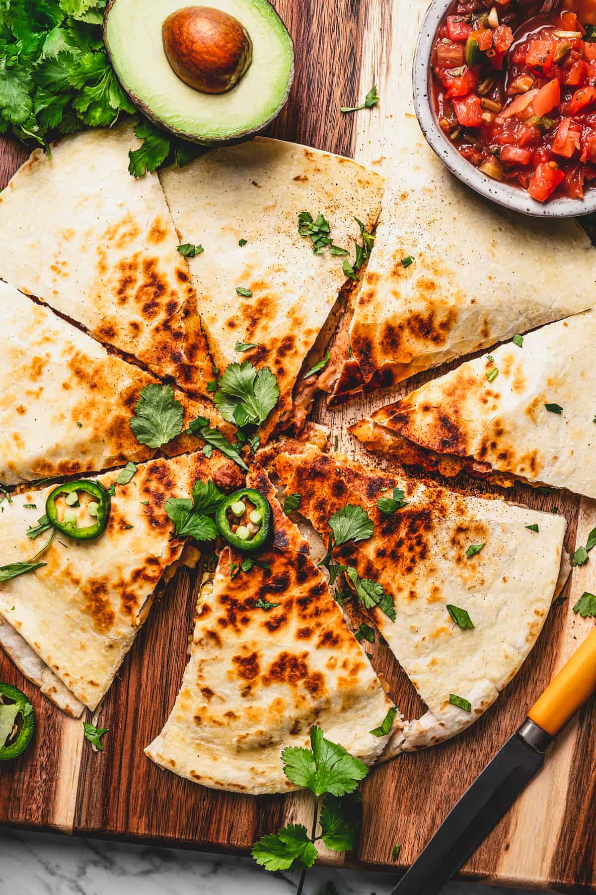 Perfectly crunchy, cheesy breakfast quesadillas stuffed with breakfast favorites like scrambled eggs, refried beans, bacon, and potatoes. overhead shot of sliced quesadillas topped with cilantro and jalapeno slices.