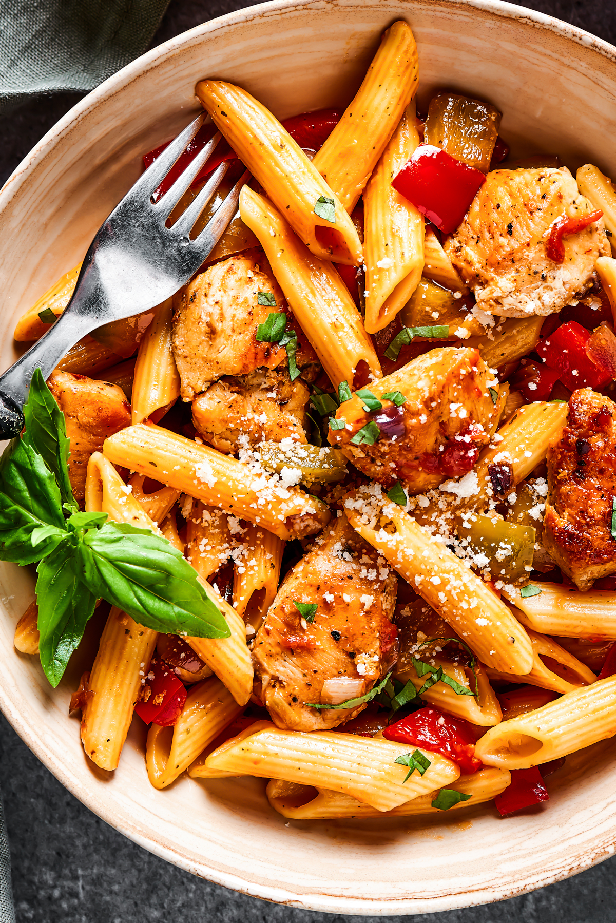 Cooked penne pasta and bite-sized chicken pieces in a bowl.