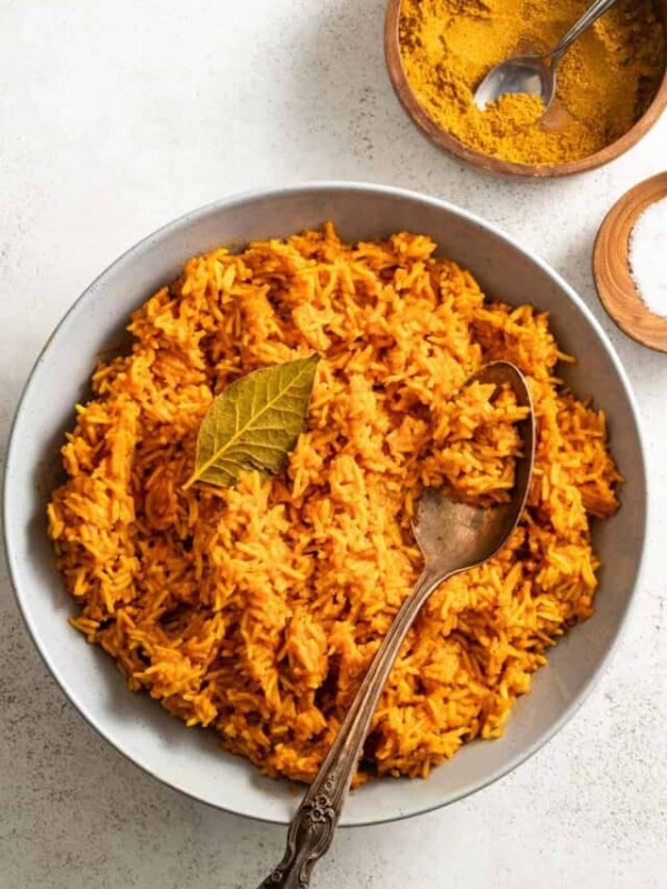 Jollof rice in a bowl with a spoon, topped with a bay leaf.