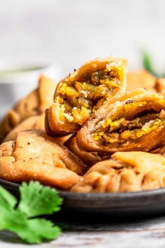 A bowl filled with samosas, and a samosa cut in half with the filling exposed.