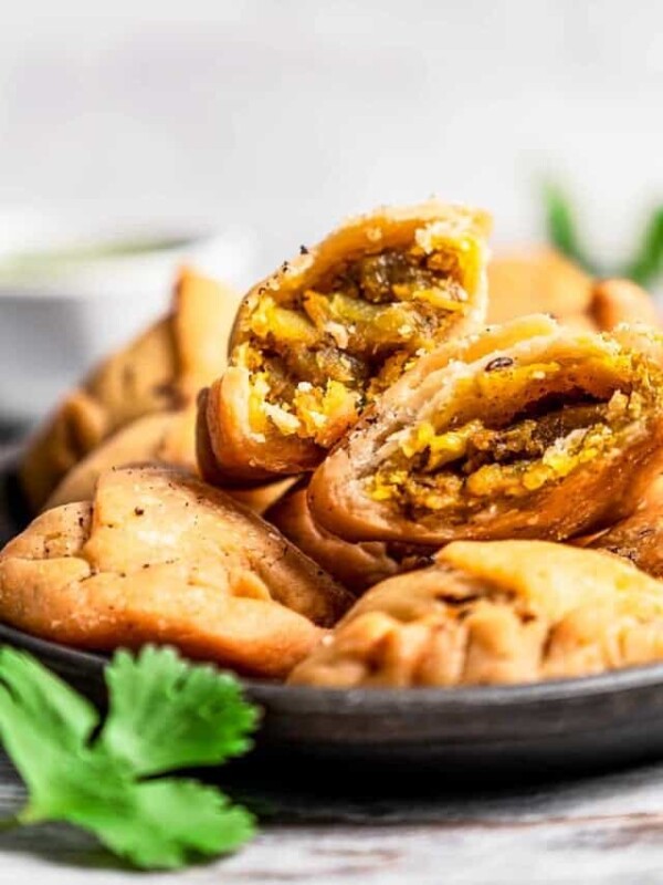 A bowl filled with samosas, and a samosa cut in half with the filling exposed.