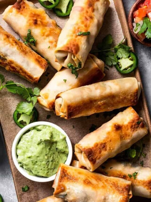 Overhead shot of a sheet pan with Homemade egg rolls and a bowl of avocado crema on the side.