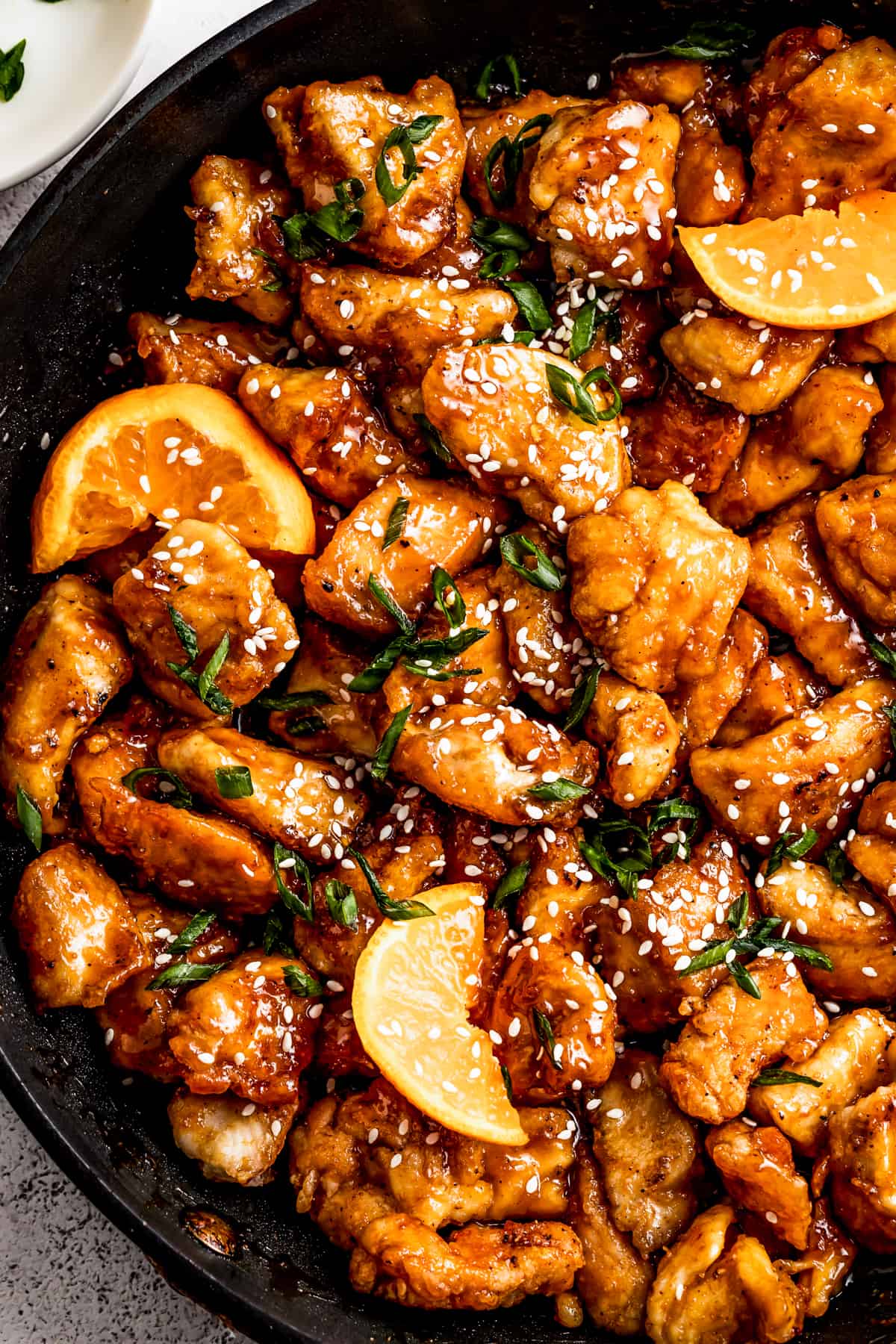 mandarin chicken in a pan, garnished with orange slices, green onions, and sesame seeds.