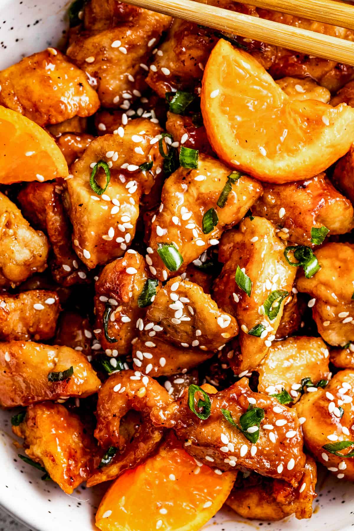 up close shot of mandarin chicken in a bowl, garnished with orange slices, green onions, and sesame seeds.
