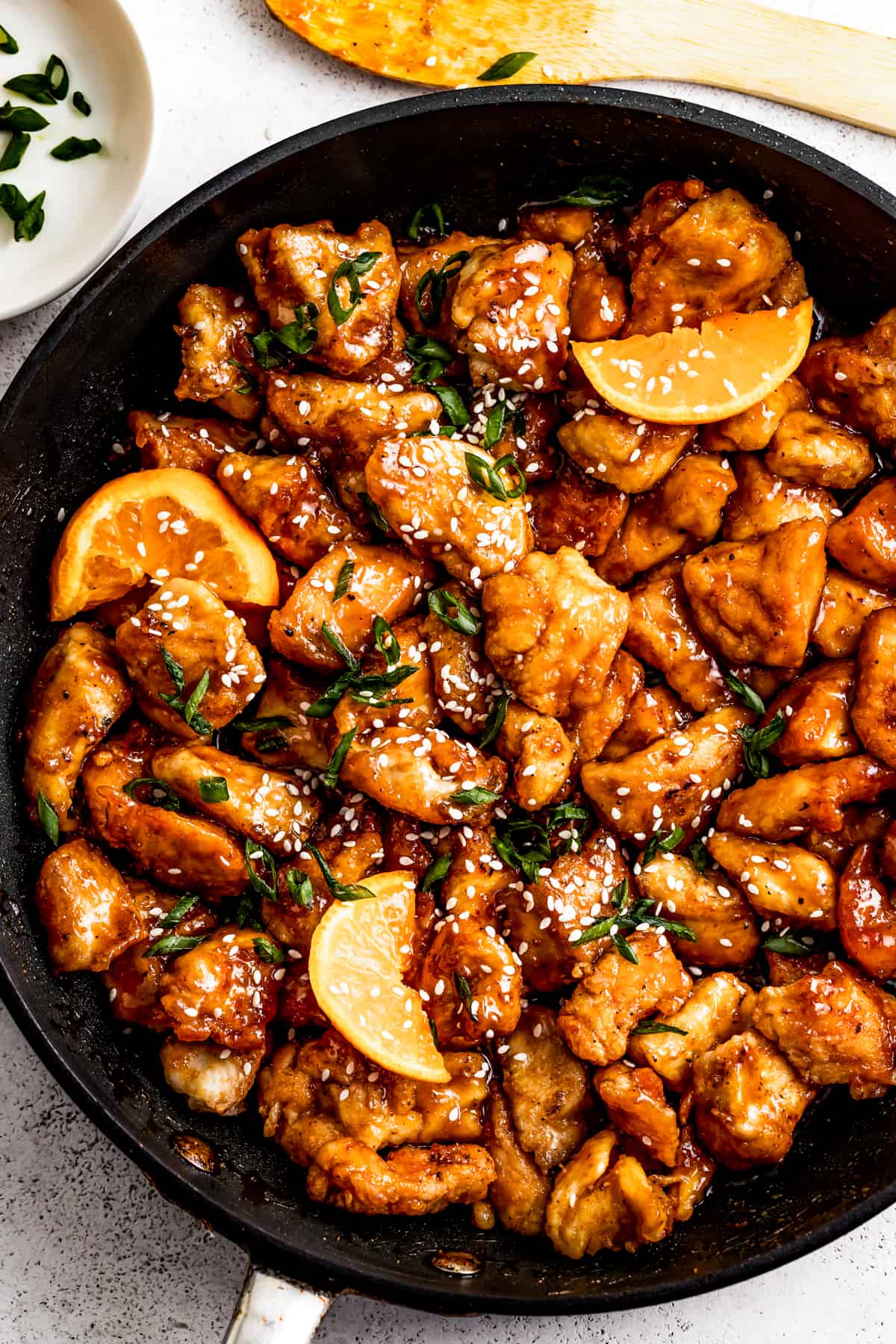 mandarin chicken in a pan, garnished with orange slices, green onions, and sesame seeds.