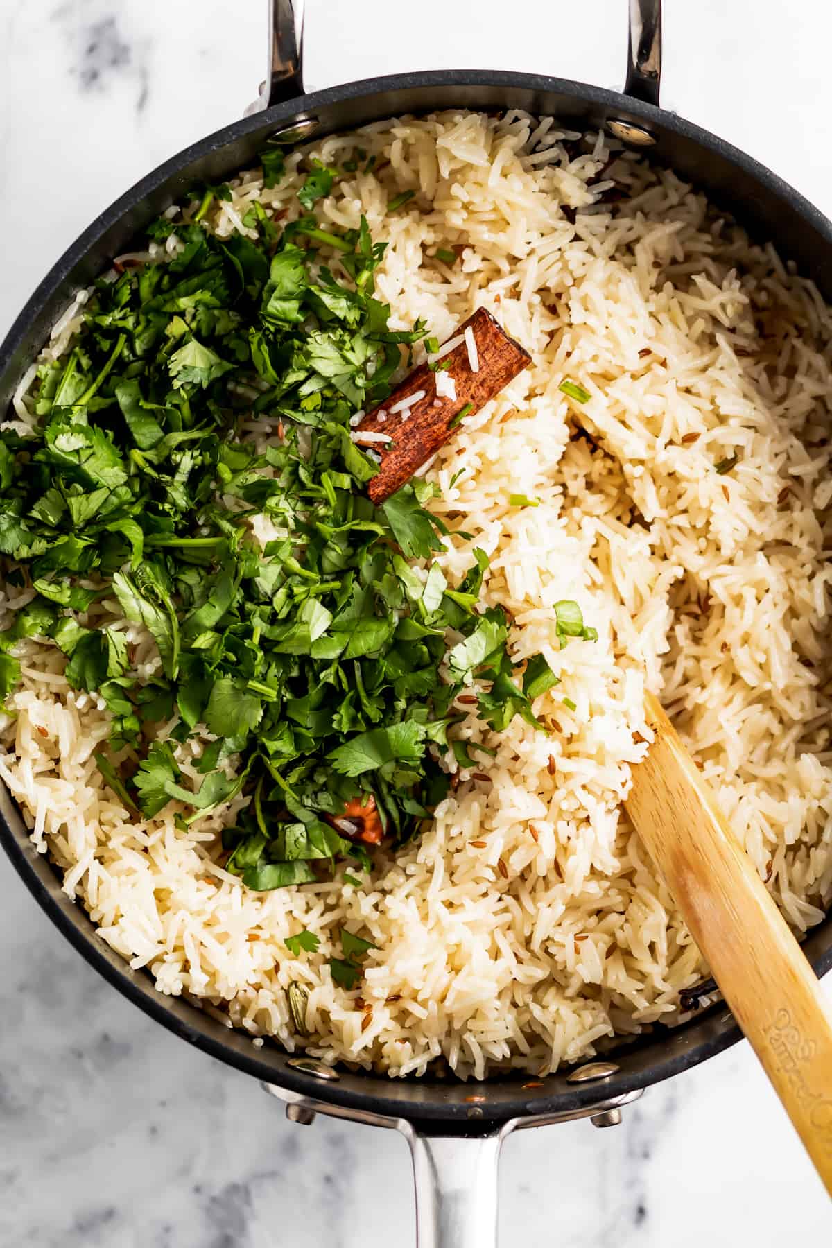 Adding fresh coriander to a skillet filled with rice.