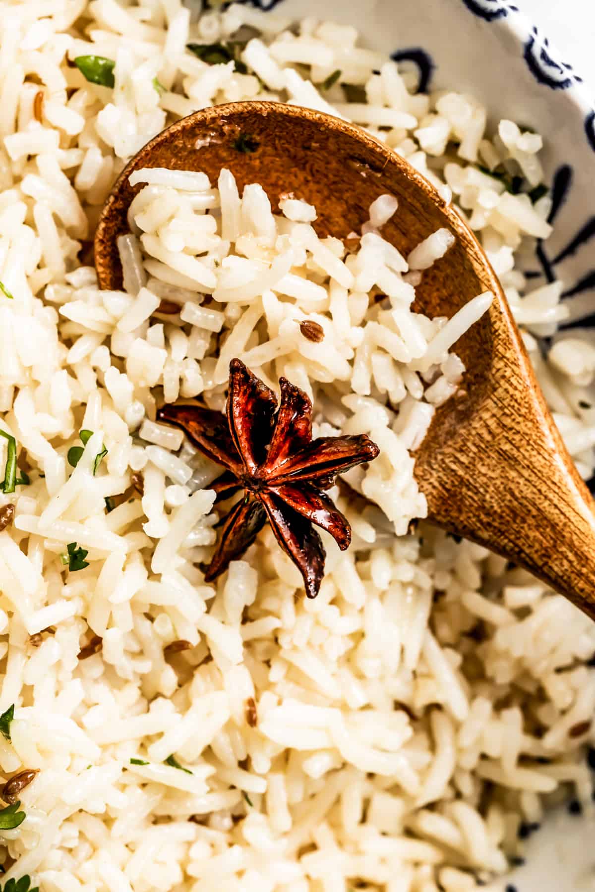 Close-up of cumin rice garnished with star anise and a wooden spoon placed in the rice.