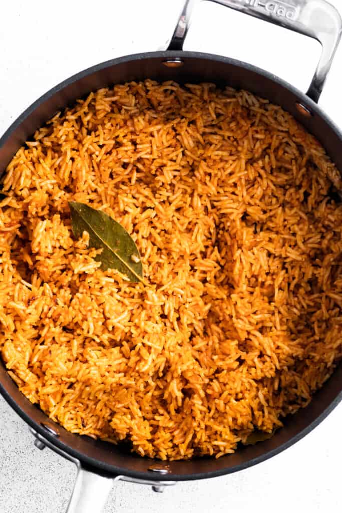 Jollof rice in a saucepan with a spoon and a bay leaf.