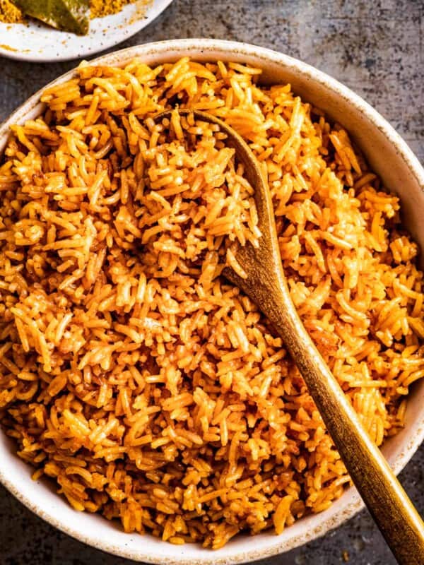 Jollof rice in a serving bowl with a spoon and a bay leaf.