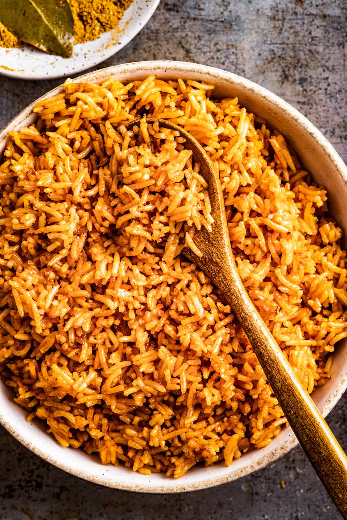 Jollof rice in a serving bowl with a spoon and a bay leaf.