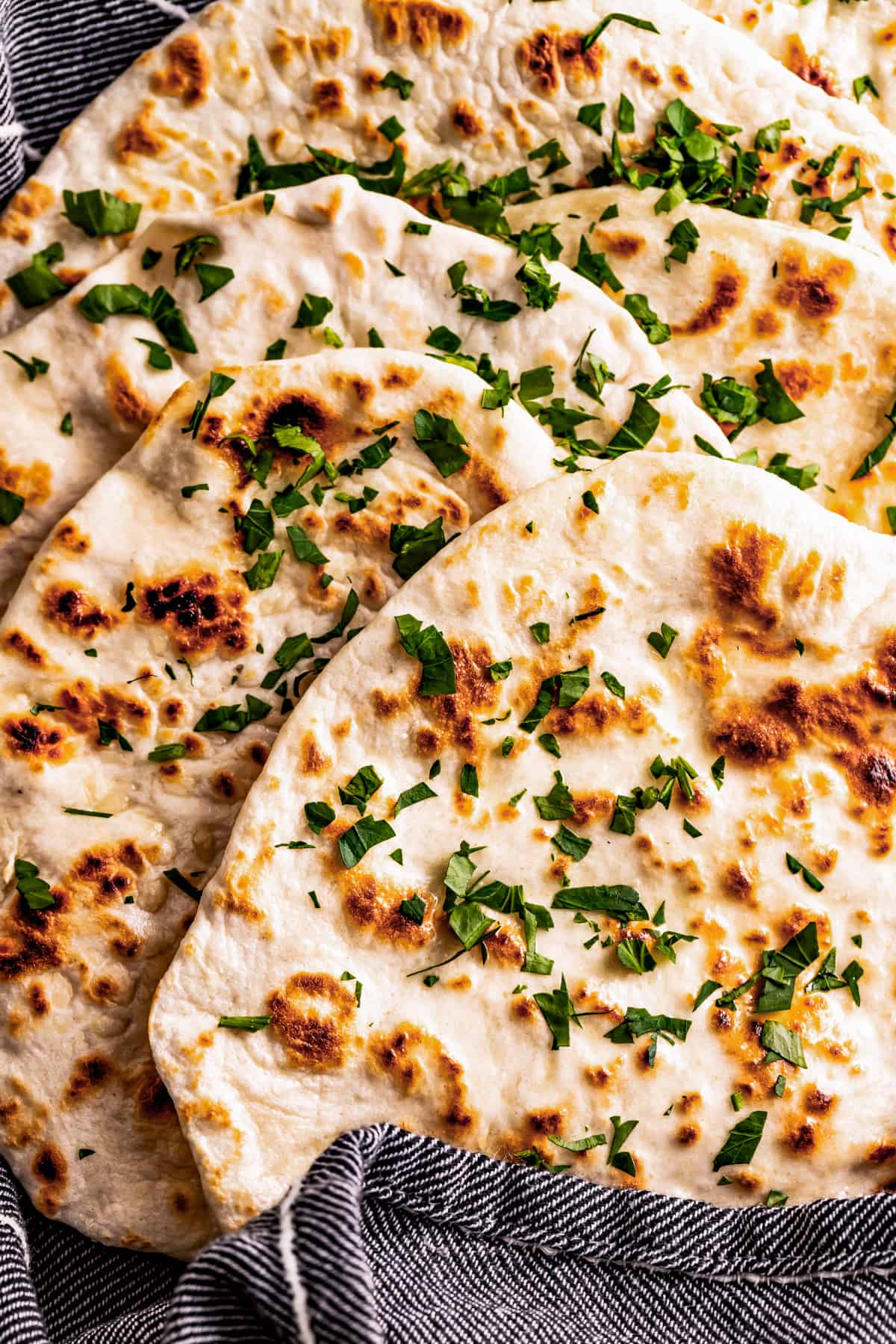 lavash flatbreads garnished with parsley and stacked in a gray kitchen towel.