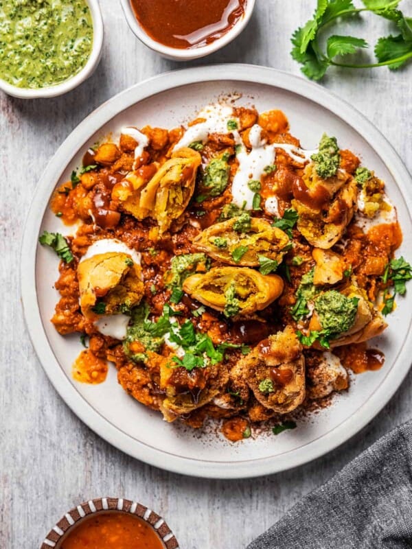 overhead shot of samosa chaat on a plate, with small bowls with sauces placed around the plate.