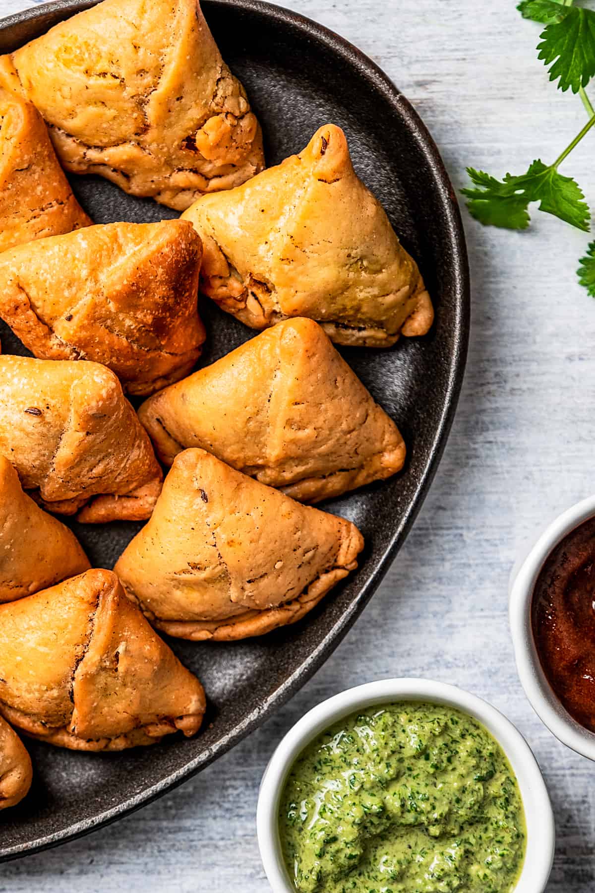 Homemade samosas on a plate, with two small bowls of chutney placed next to the plate.