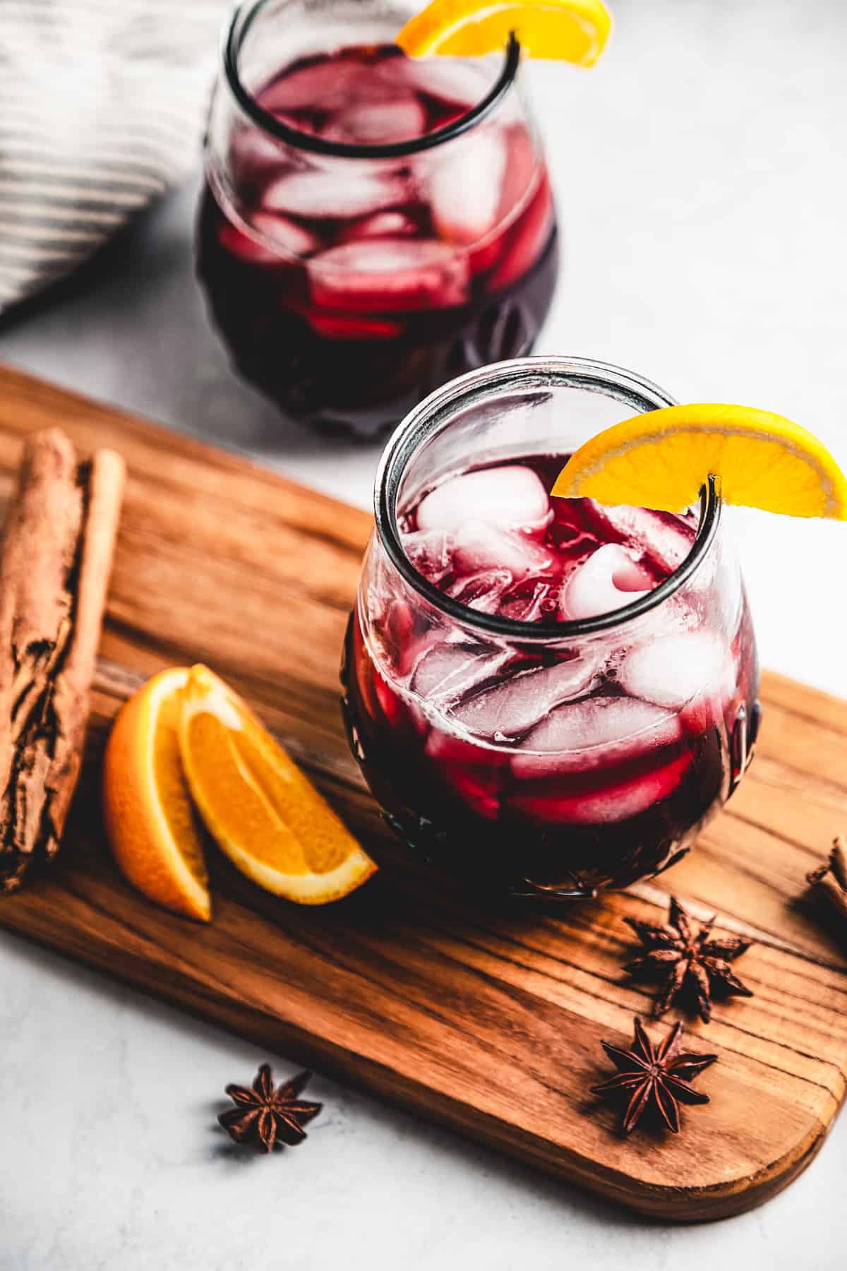 Jamaican sorrel in a glass with ice placed on a wooden board with star anise and orange slices arranged around the glass.