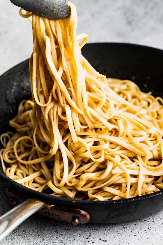 Gently tossing the noodles in the pan with tongs.