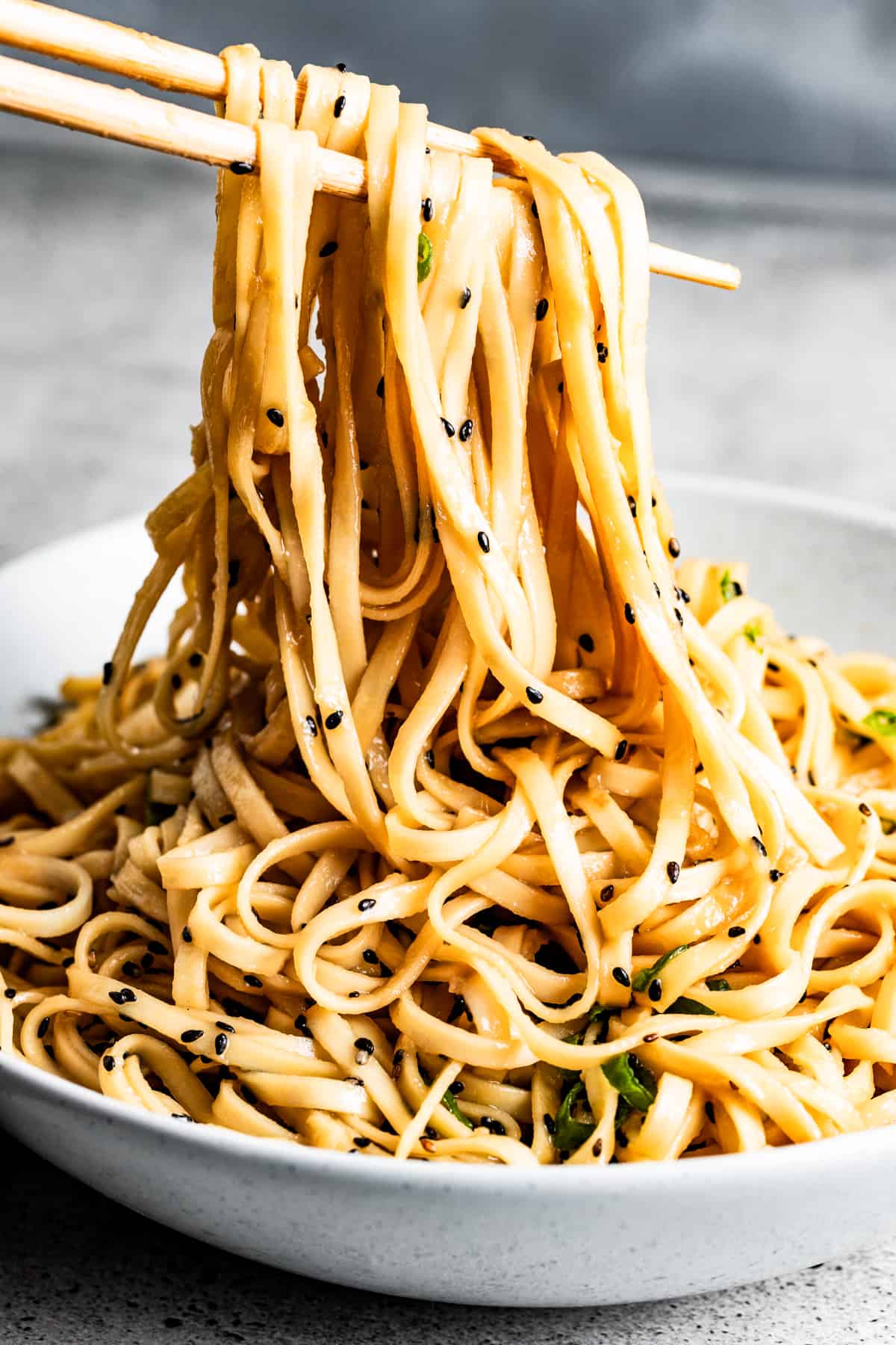 Lifting teriyaki noodles from the bowl with chopsticks.