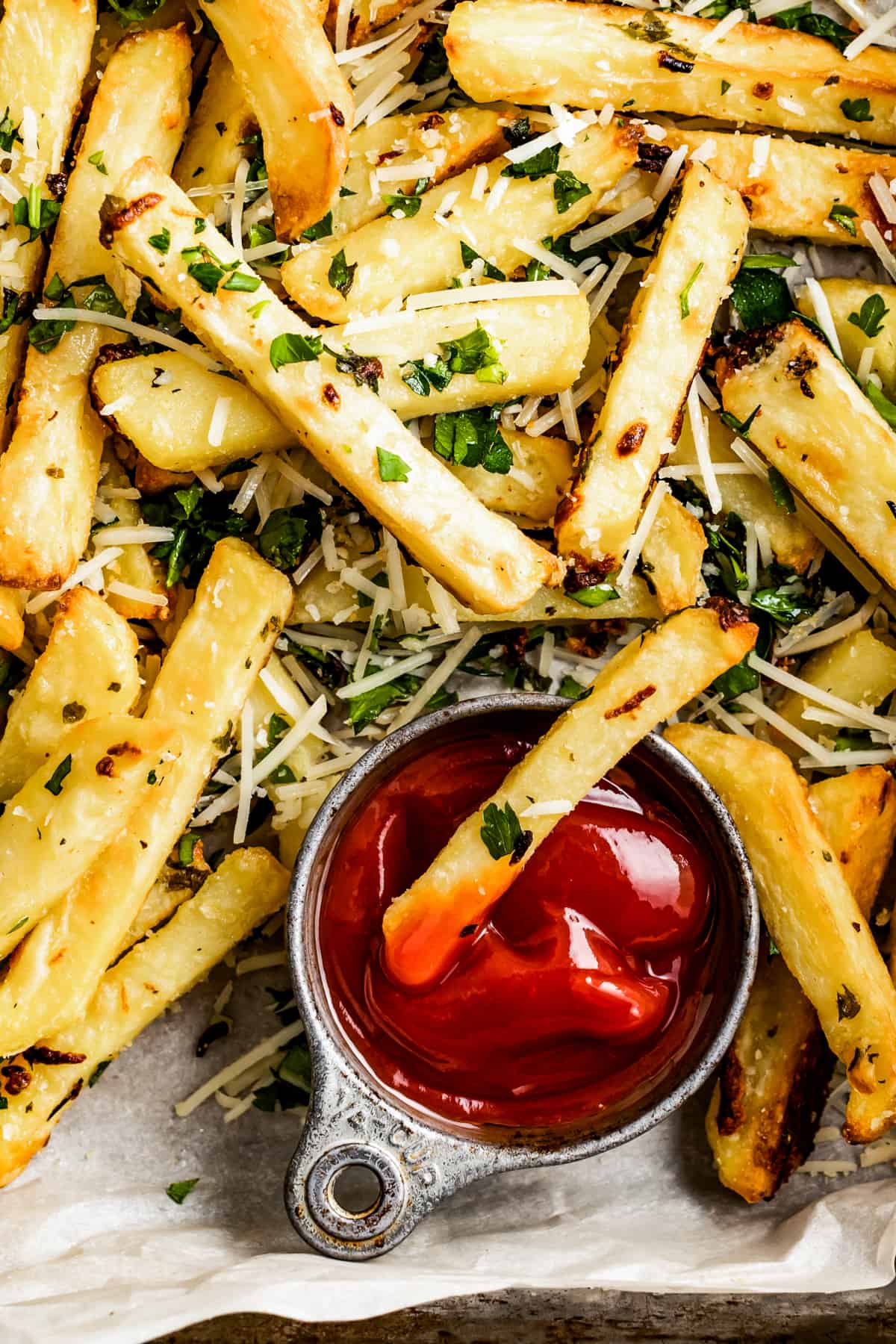 Parmesan truffle fries are arranged on a white background. One fry is dipped in a small bowl of ketchup.