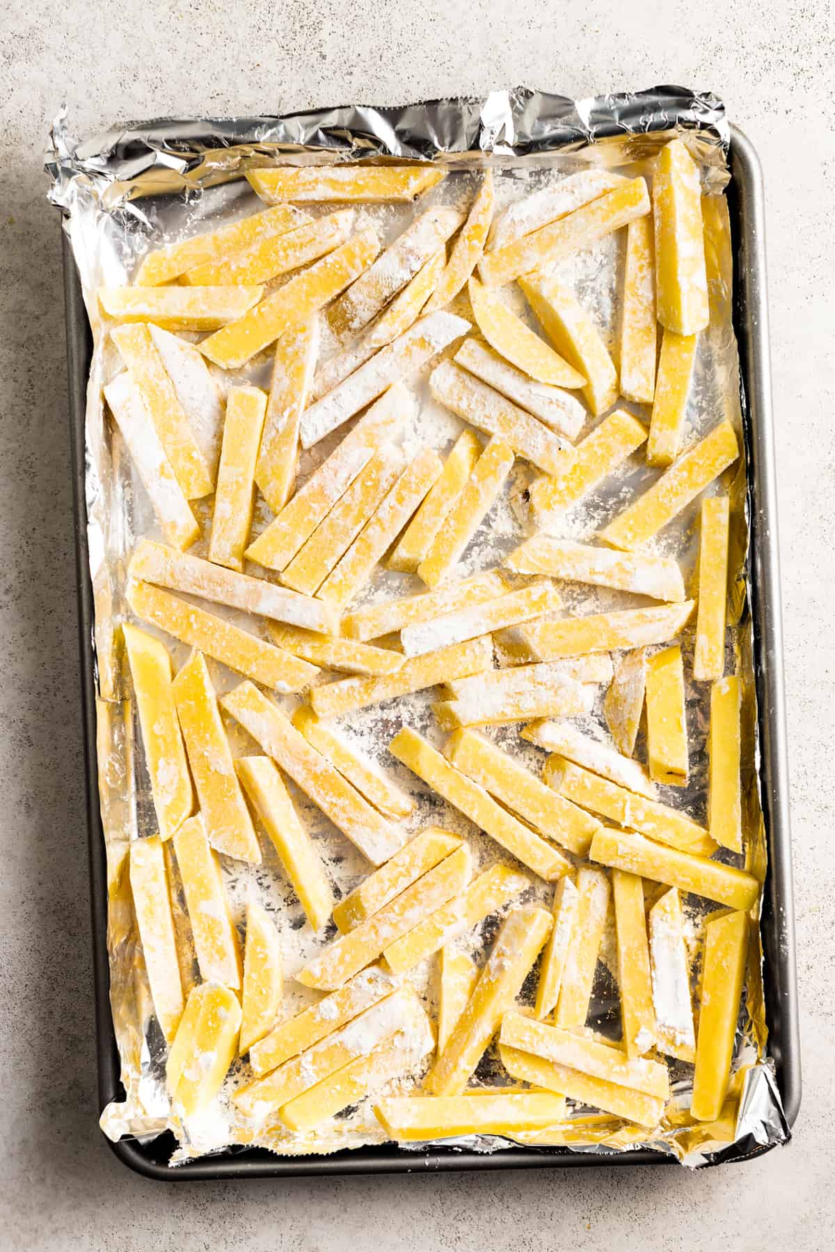 Potatoes are cut into fries and arranged on a baking sheet.