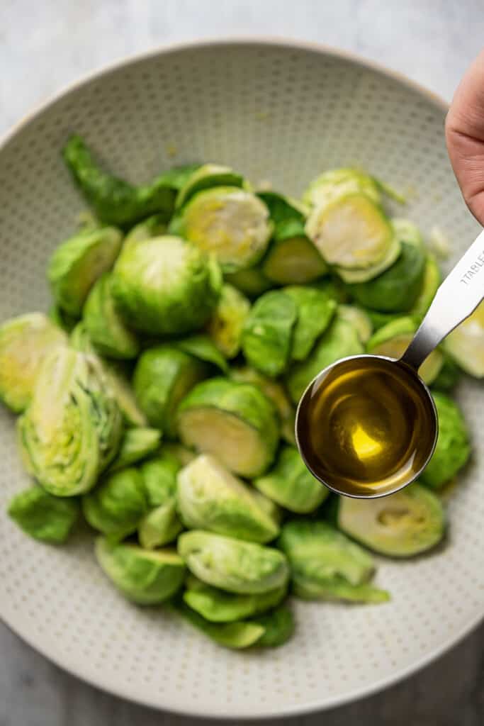 Adding olive oil to Brussels sprouts in a mixing bowl.