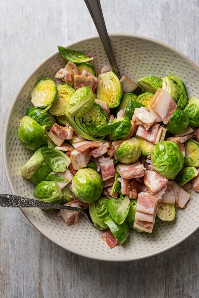 Tossing Brussels sprouts, bacon, olive oil, salt, and pepper together in a mixing bowl.
