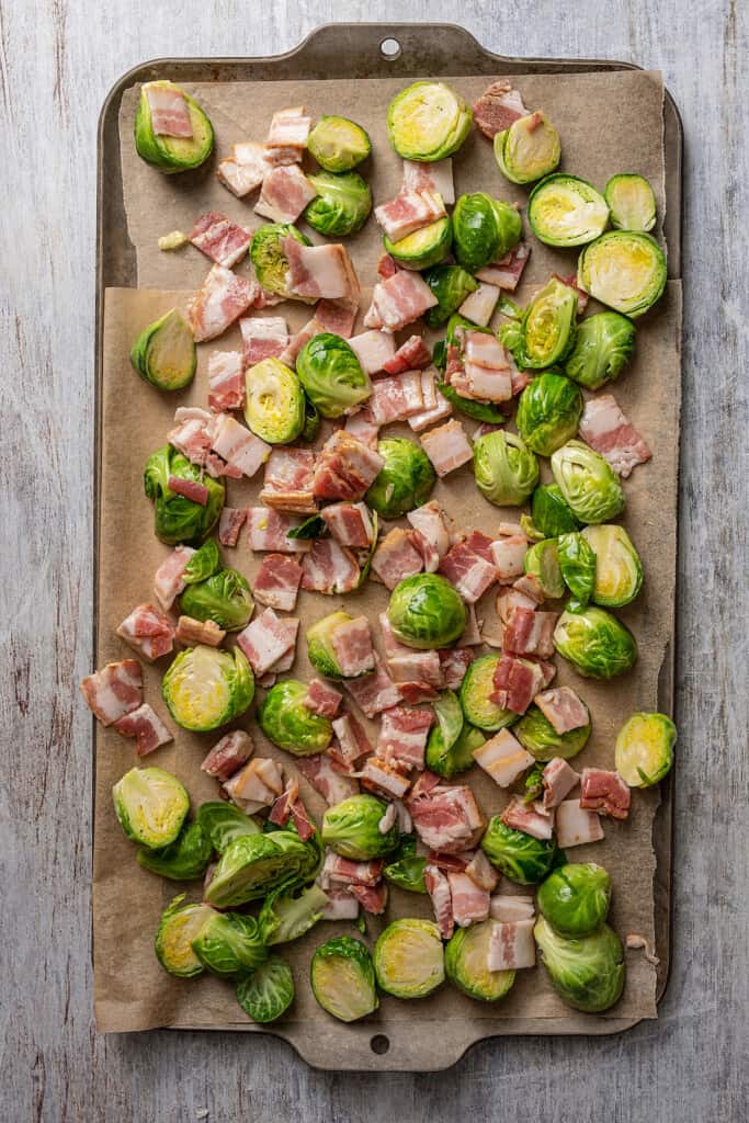 Brussels sprouts and bacon on a sheet pan ready to be baked.
