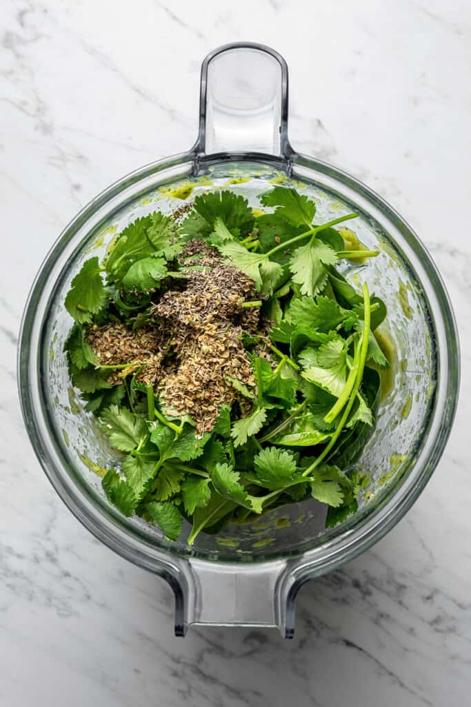 Adding oregano, thyme, cilantro, and spinach to verde sauce in a blender.
