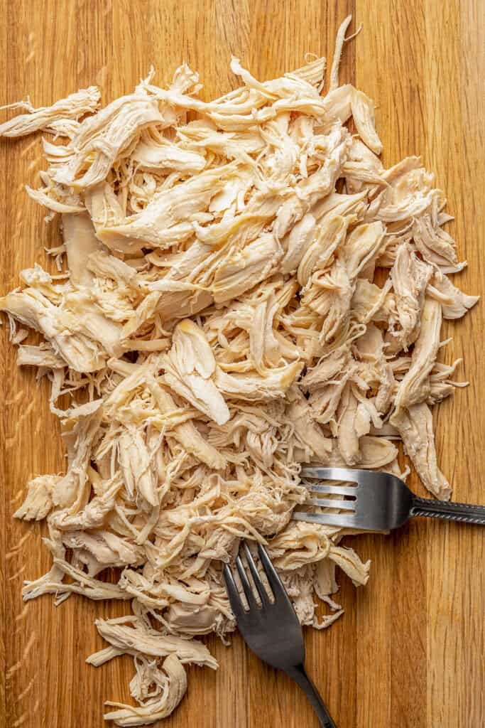 Shredding chicken on a cutting board with two forks.