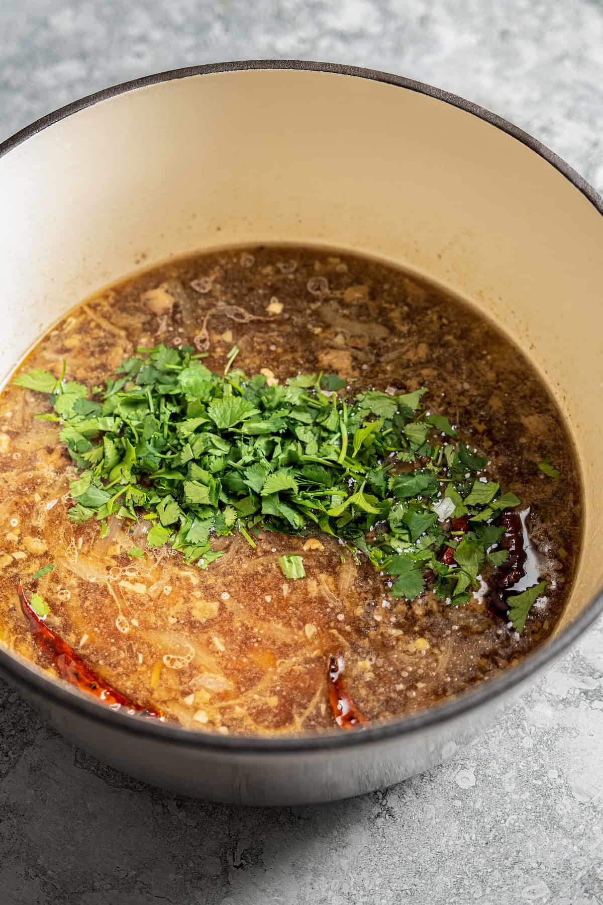 Adding cilantro to a pot full of broth, chilis, and white corn kernels.