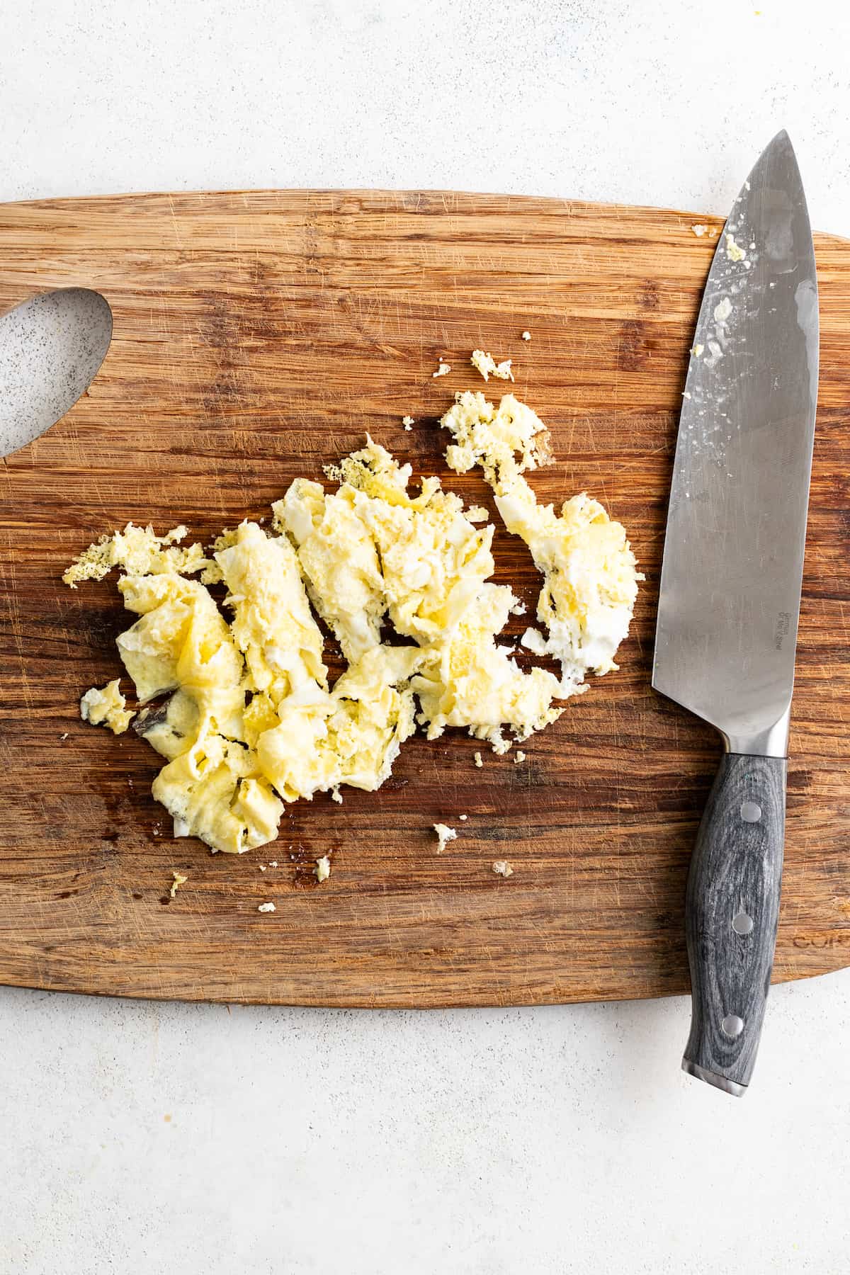 Chopping cooked scrambled eggs on a cutting board.