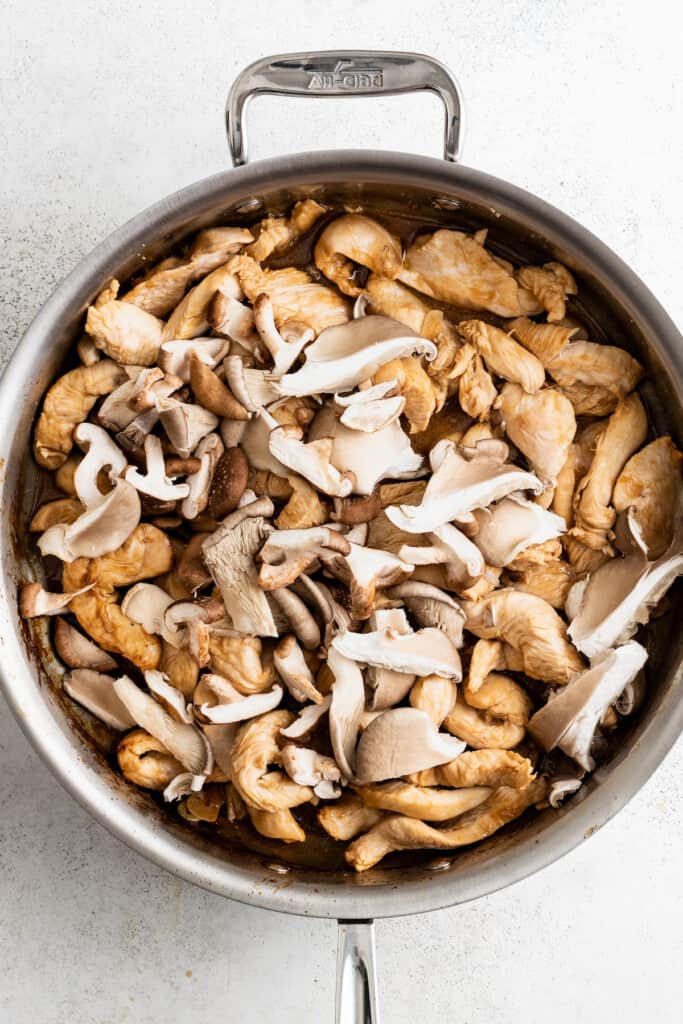 Adding shitake mushrooms to a pan with crowned chicken.